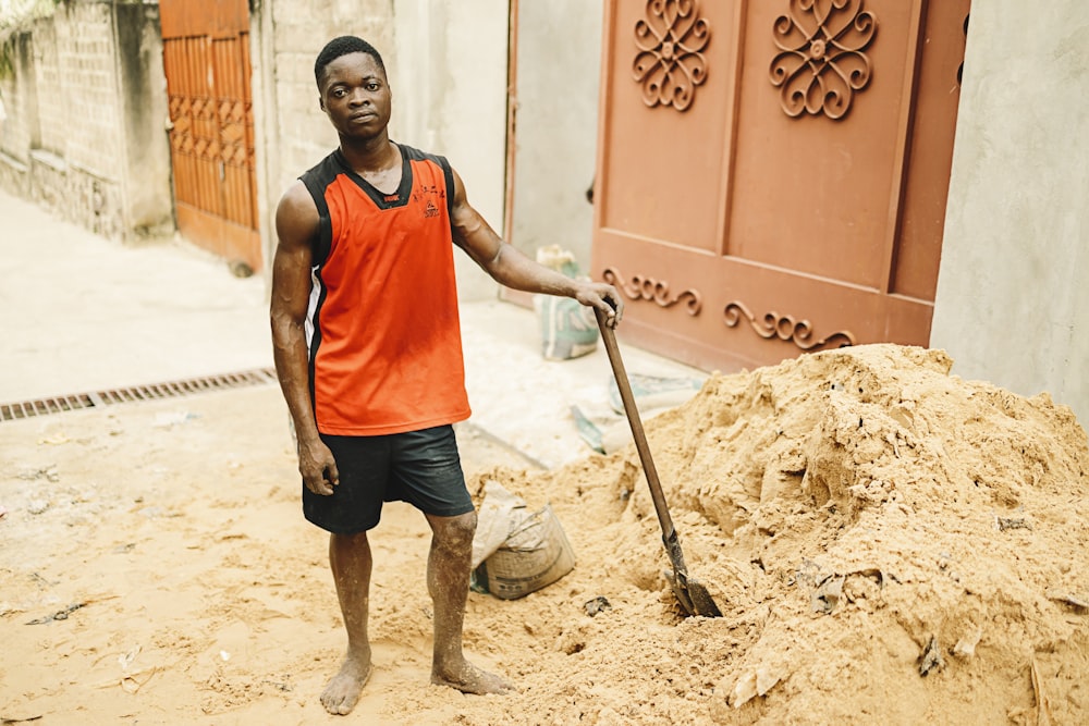 man in red tank top and black shorts holding shovel