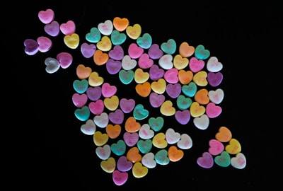 A collection of pastel-colored heart-shaped candies with short messages printed on them, arranged in a unique pattern against a black background.