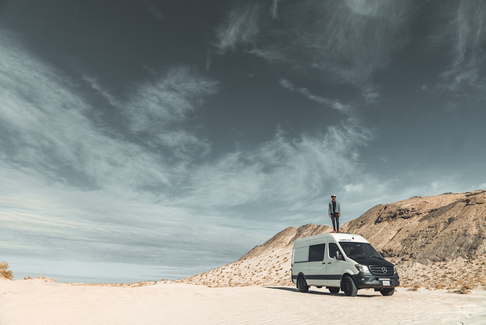 man standing on white suv on brown sand under blue sky during daytime