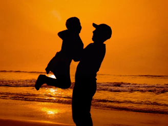 An intimate moment of a parent lifting their child against a backdrop of sandy tones and golden hour light
