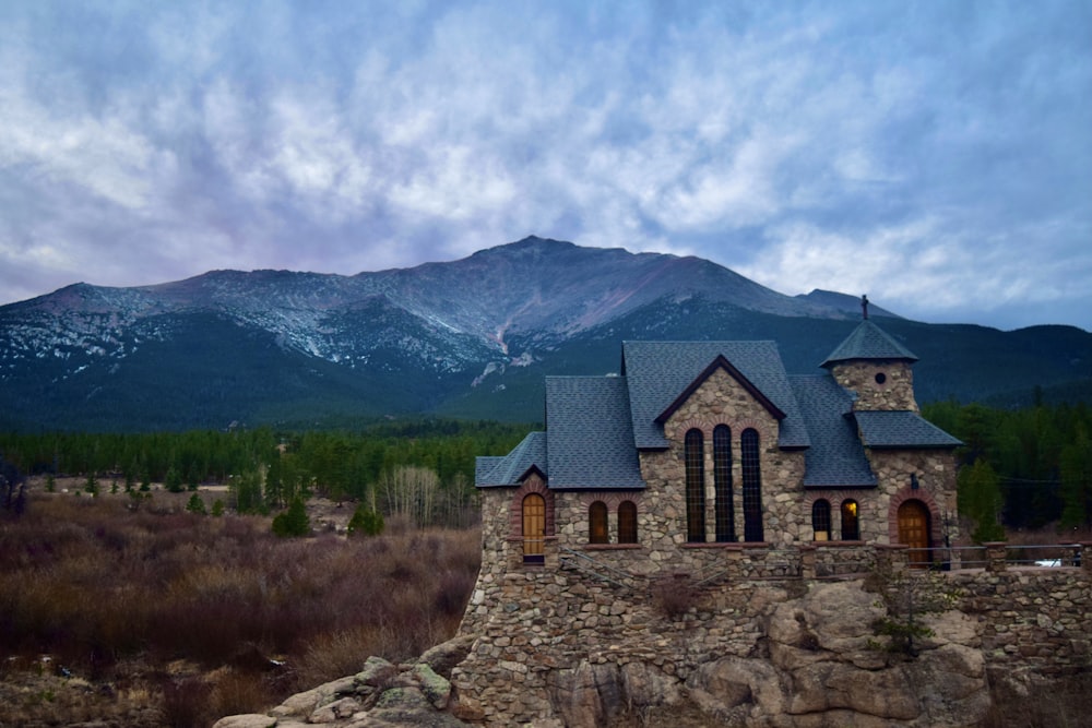 brown brick building near green grass field and mountain under white clouds and blue sky during