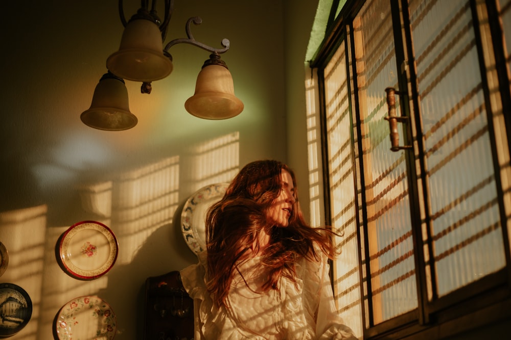 woman in white long sleeve shirt standing beside window