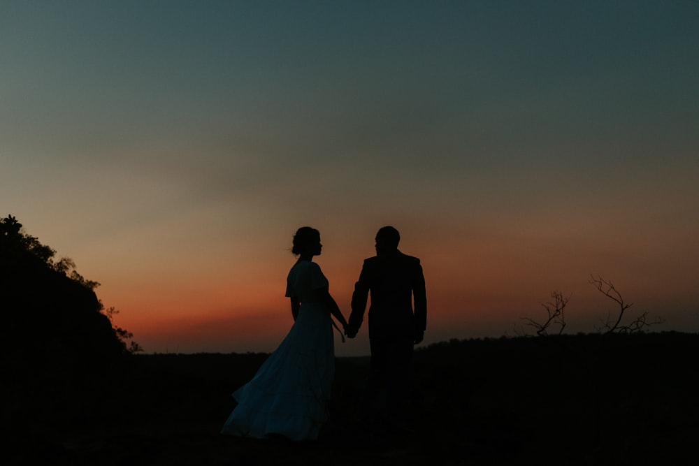 man and woman standing on grass field during sunset