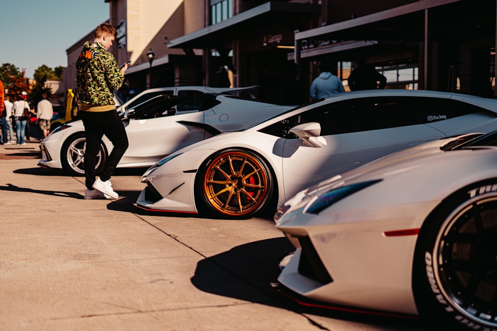 man in black and white jacket standing beside white lamborghini aventador