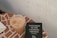 A mosaic-tiled surface holds a plastic cup of iced coffee next to a book titled 'Catechism of the Catholic Church, Second Edition'. The background features a neutral-toned wall.