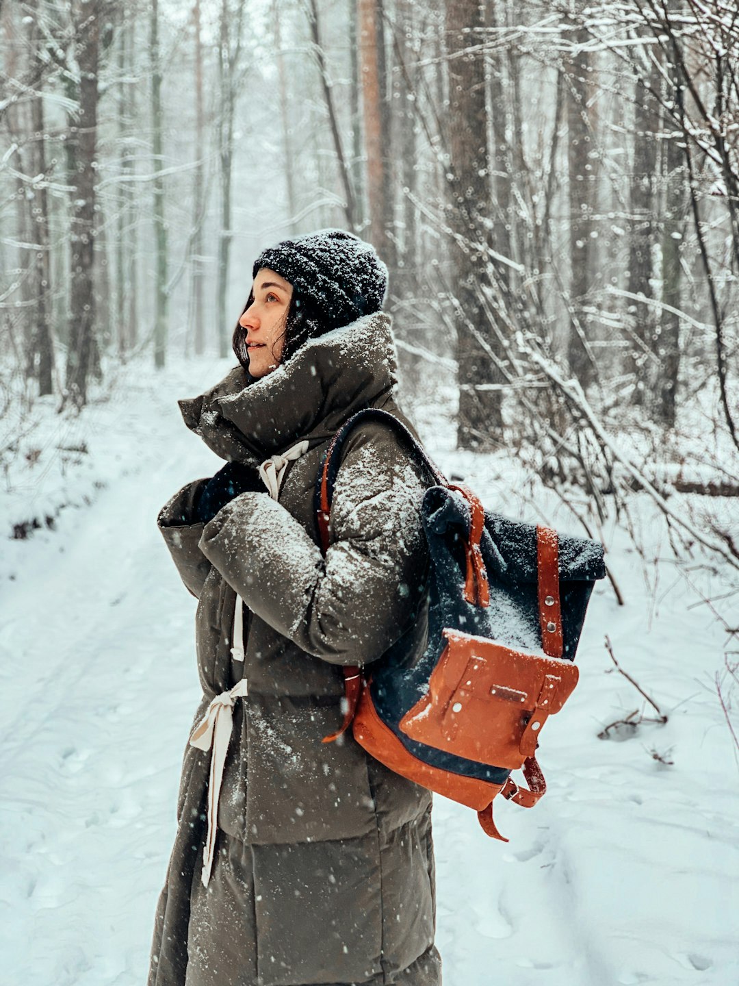 woman in brown coat and gray knit cap carrying brown leather backpack on snow covered ground