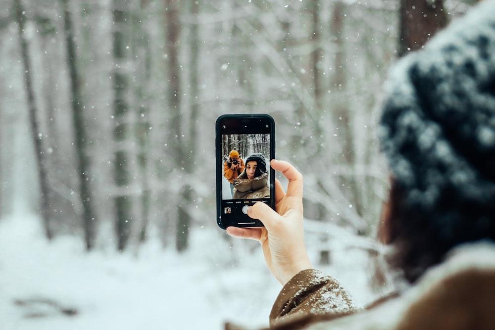 person holding black iphone 5 taking photo of snow covered trees during daytime