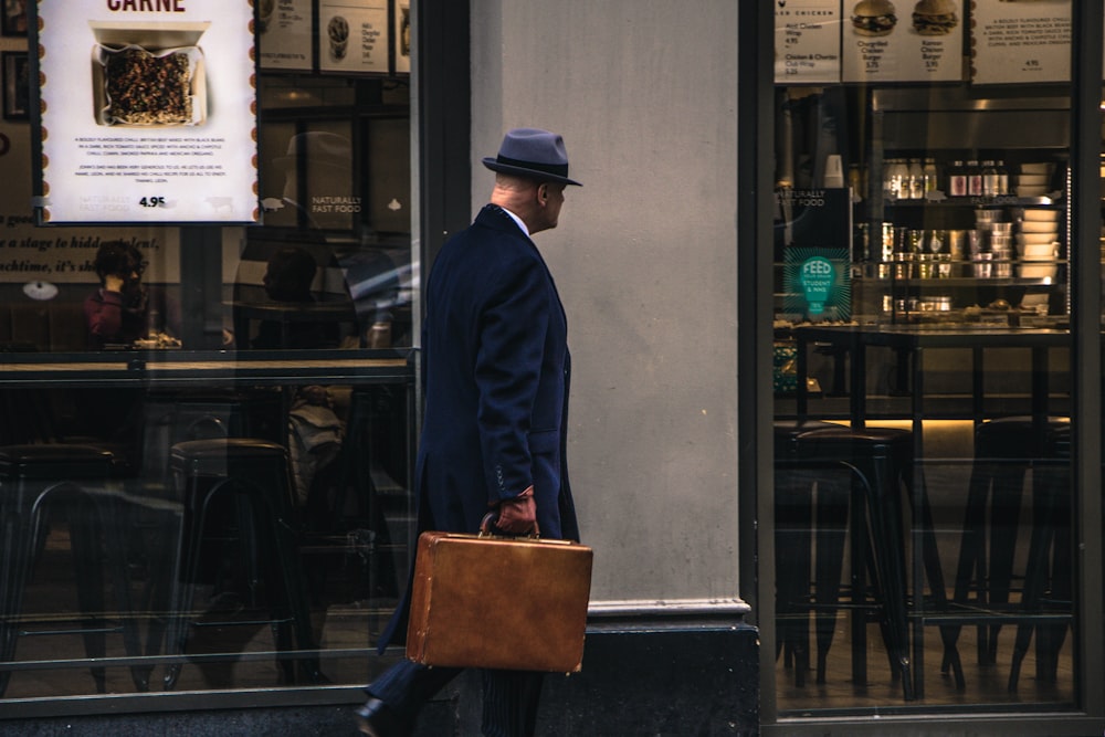 검은 양복 재킷과 파란 모자를 쓴 남자가 가게 앞에 서 있다