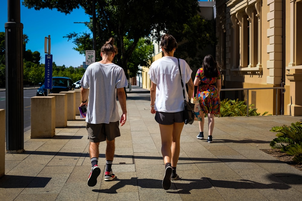 man in white crew neck t-shirt and black shorts walking on sidewalk during daytime