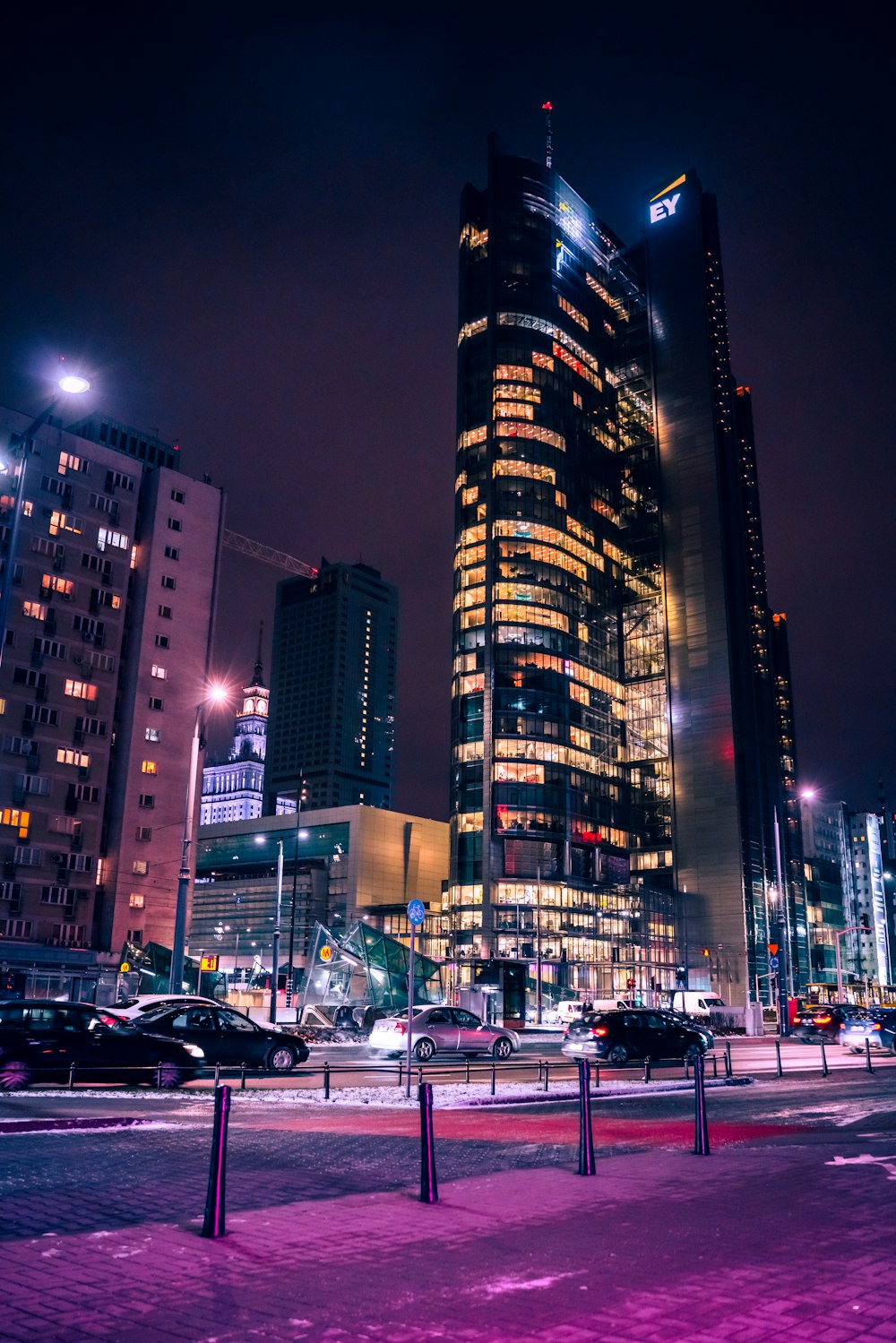 cars parked on side of road near high rise building during night time