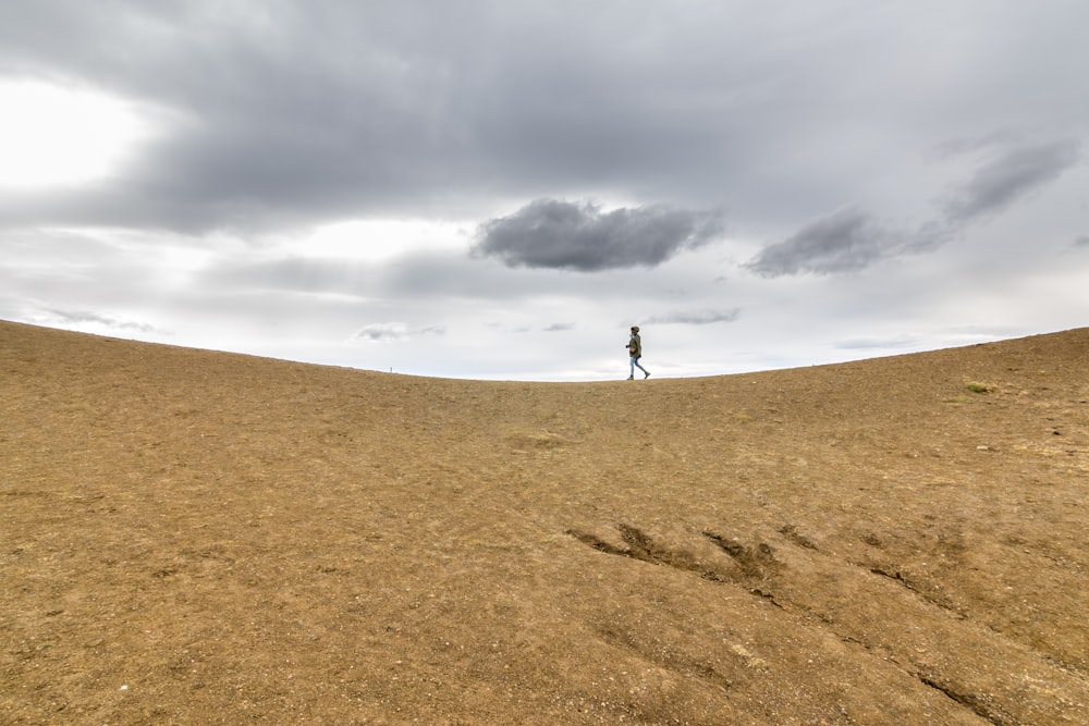 person walking on brown sand under white clouds during daytime