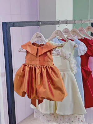 A colorful kids' Muslim dress hanging on a wooden rack with soft natural lighting highlighting the fabric details.