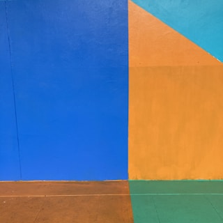 A geometric abstract composition featuring bold blocks of color. The left half is dominated by a large blue rectangle while the right combines a mustard yellow square with a smaller teal triangle above. The lower portion has a narrow strip of green and orange, creating a visually striking contrast.