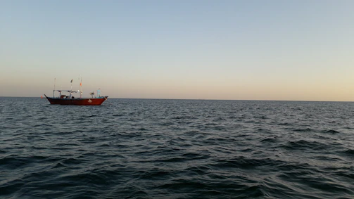 A calm sea with a fishing boat preparing for a trip at sunrise.