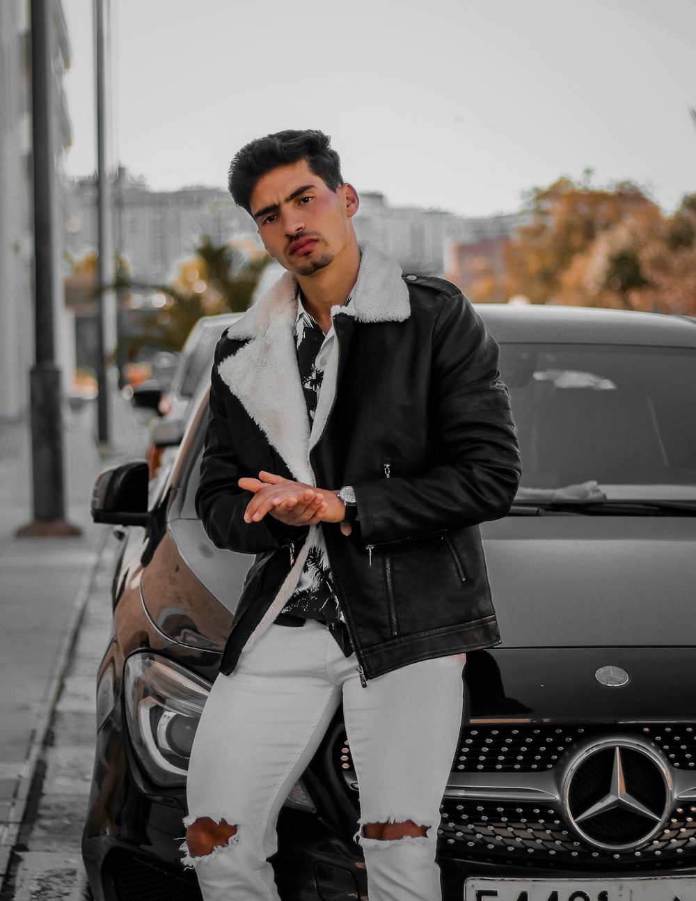 man in black suit jacket and white pants sitting on silver car