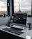 A modern workspace with a large computer monitor on a sleek white desk. Various desk accessories, including a lamp, speakers, and a smartphone stand, are neatly arranged. Through the large window, the Eiffel Tower is visible against a cloudy sky, offering a scenic city view.