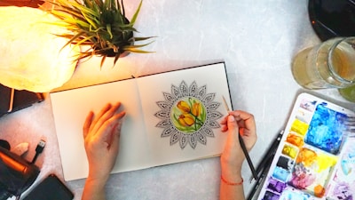 Close-up of hands coloring in a mindfulness activity book surrounded by fresh leaves.