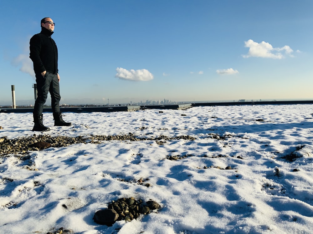 hombre en chaqueta negra de pie en el campo cubierto de nieve bajo el cielo azul durante el día