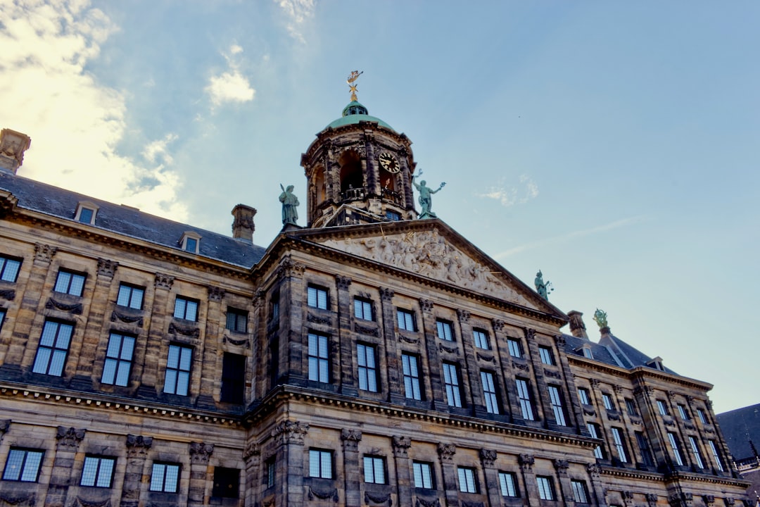 brown concrete building under blue sky during daytime, Vista inclinada do Palácio Real de Amesterdão (https://www.paleisamsterdam.nl/en/about-palace/) com cúpula e estátuas envolvidas pela céu. // Slanted view of the Royal Palace Amsterdam with dome and statues surrounded by the sky.<p></figure>