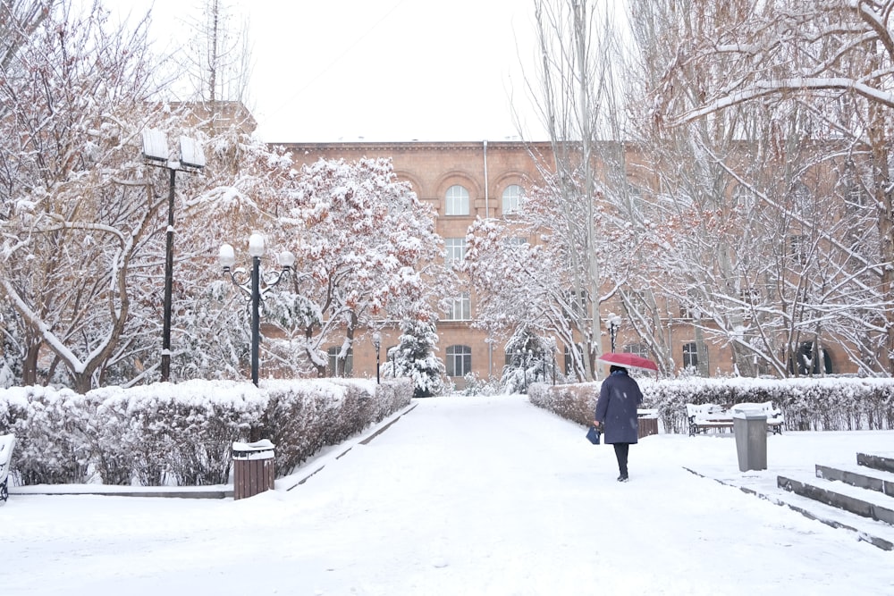 person in red jacket walking on snow covered pathway