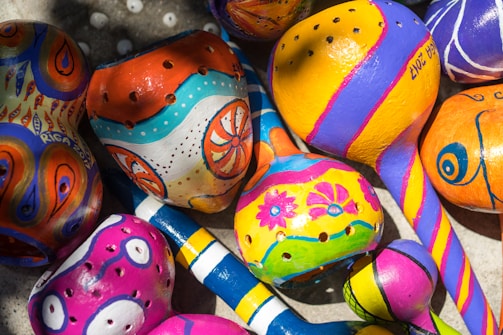 A collection of brightly painted maracas with intricate designs, featuring a mix of floral motifs and abstract patterns. The vibrant colors add a lively and artistic touch to the scene.