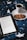 A cozy scene featuring an open ebook reader displaying text, placed on a bed or blanket with a starry pattern. Beside the ebook, there's a white cup filled with a dark beverage, likely coffee or tea, resting on a saucer. Two cookies are placed on the saucer next to the cup.