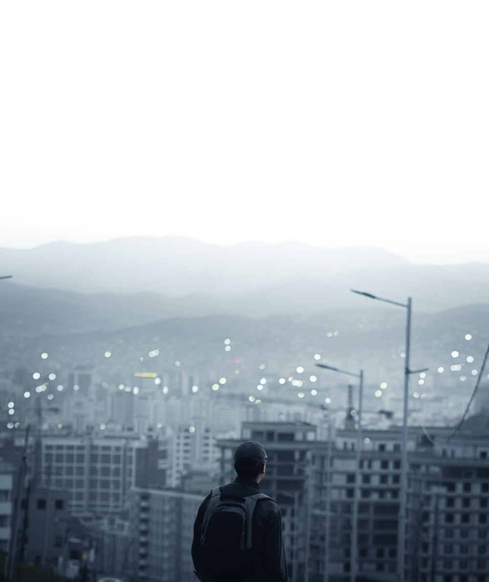 hombre en chaqueta negra de pie en la parte superior del edificio mirando los edificios de la ciudad durante el día