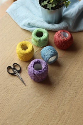 Close-up of colorful yarn, scissors, and glue sticks arranged on a wooden table.