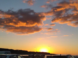 A warm amber-orange sunset casting a glow over a freshly detailed car parked by the ocean.