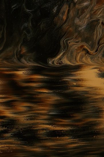 An abstract composition featuring swirling patterns and fluid textures. The image features a blend of rich, dark earthy tones with lighter, golden highlights. The textures give an impression of fluid motion, resembling a flowing liquid or an artistic representation of a landscape.