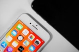 Two smartphones are shown, with one displaying a colorful home screen featuring various app icons such as Mail, Clock, and Calendar, with vibrant orange and yellow shades. The other phone, partially visible, appears to be black.