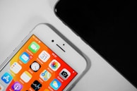 Two smartphones are shown, with one displaying a colorful home screen featuring various app icons such as Mail, Clock, and Calendar, with vibrant orange and yellow shades. The other phone, partially visible, appears to be black.