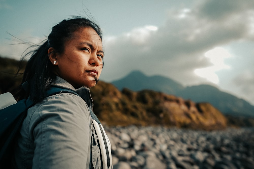 woman in grey jacket standing on grey rock during daytime