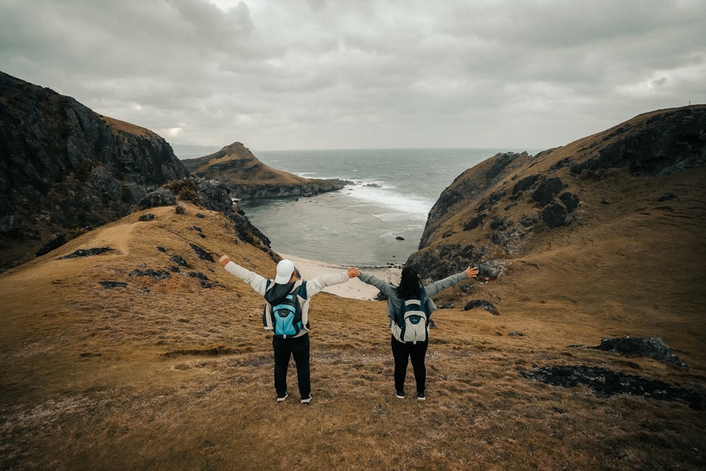 2 women standing on brown rocky mountain near body of water during daytime