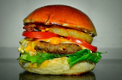 A delicious-looking burger stacked with a beef patty, fresh lettuce, cheese, slices of tomato, a ring of pineapple, bacon, and a glossy, golden-brown bun.