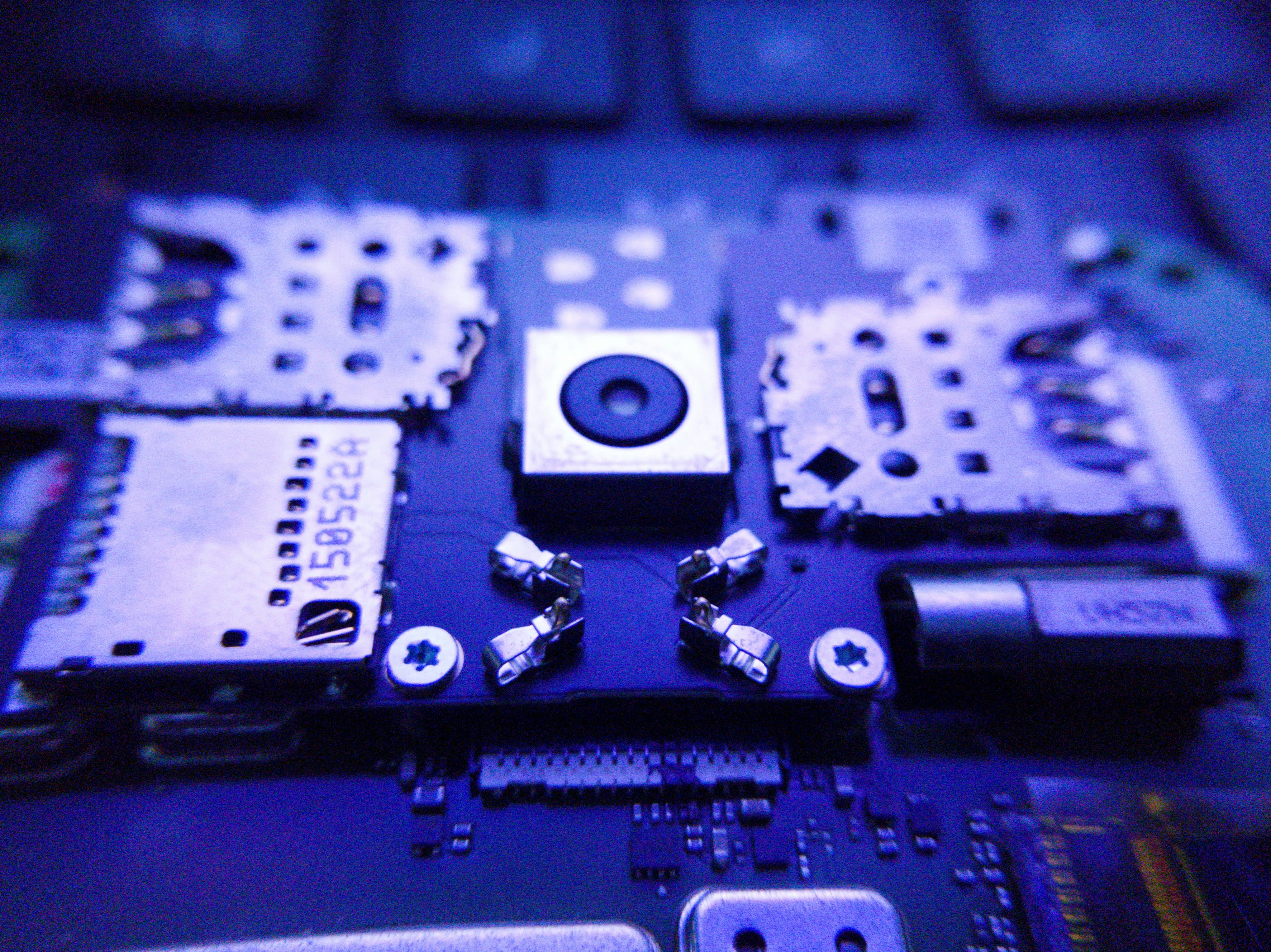 Computer chip circuit board closeup, dim blue-tinted lighting, dark background, deep shadows, electronic components