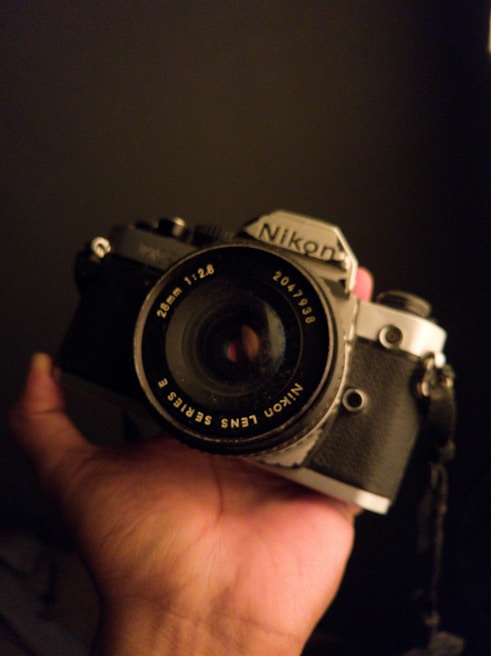 Close-up of a weathered hand gripping a vintage camera, bathed in soft, low light.