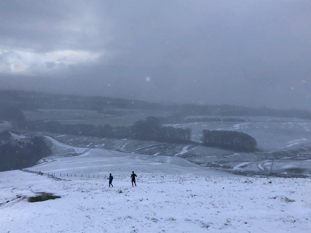 2 person walking on snow covered field during daytime