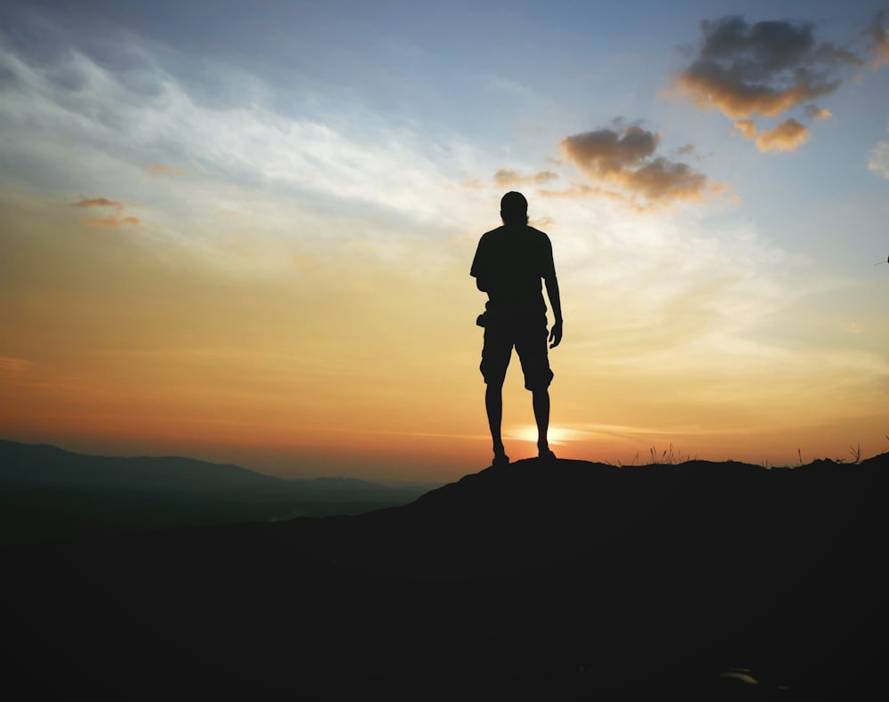 Silueta del hombre de pie en la cima de la montaña durante la puesta del sol