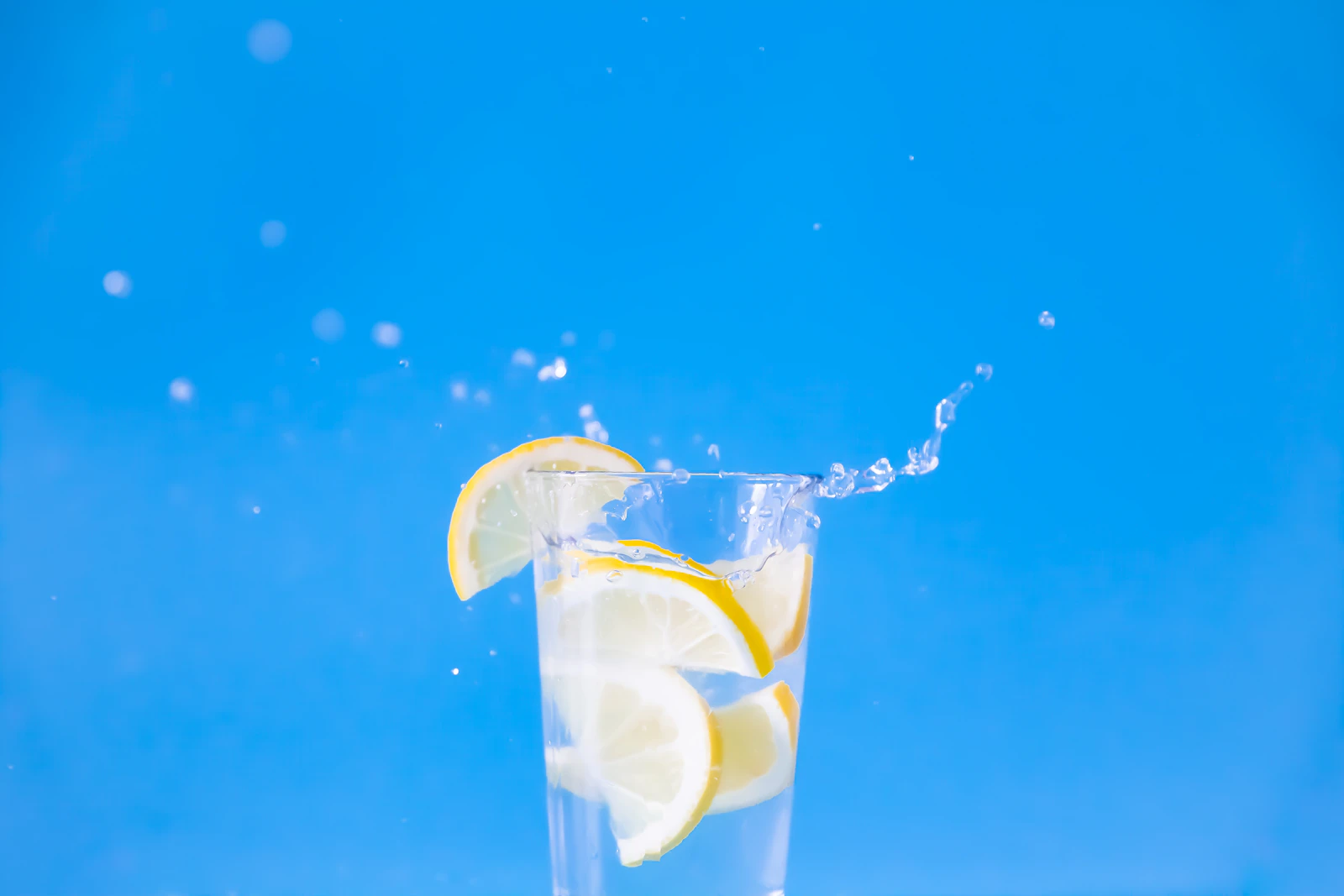 A glass of water with a lemon slice against a blue background