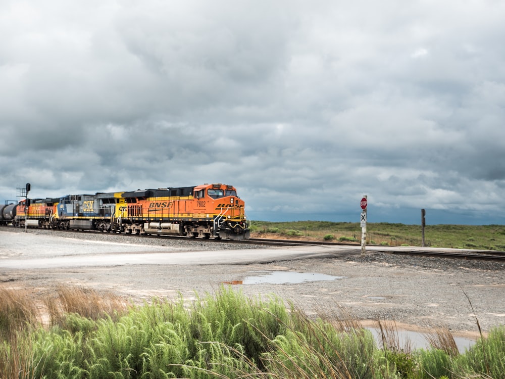 orange and black train on rail road under cloudy sky during daytime