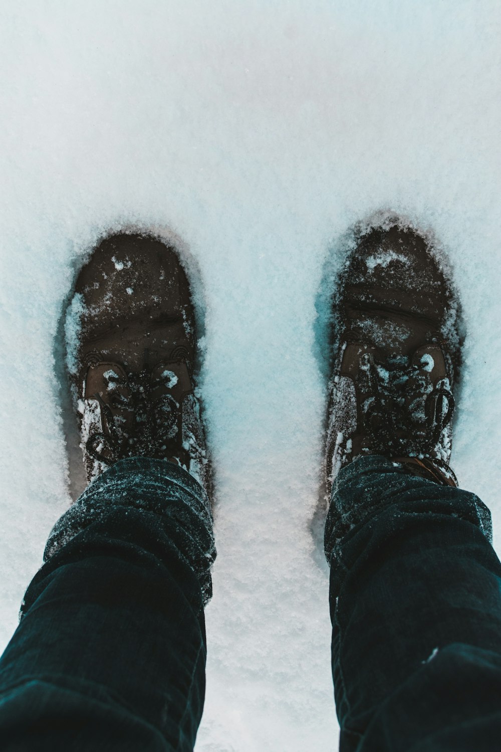 personne en pantalon noir et chaussures noires debout sur un sol enneigé