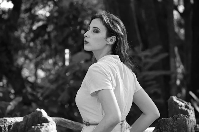 Portrait of a thoughtful woman in a natural setting with soft light and greenery.