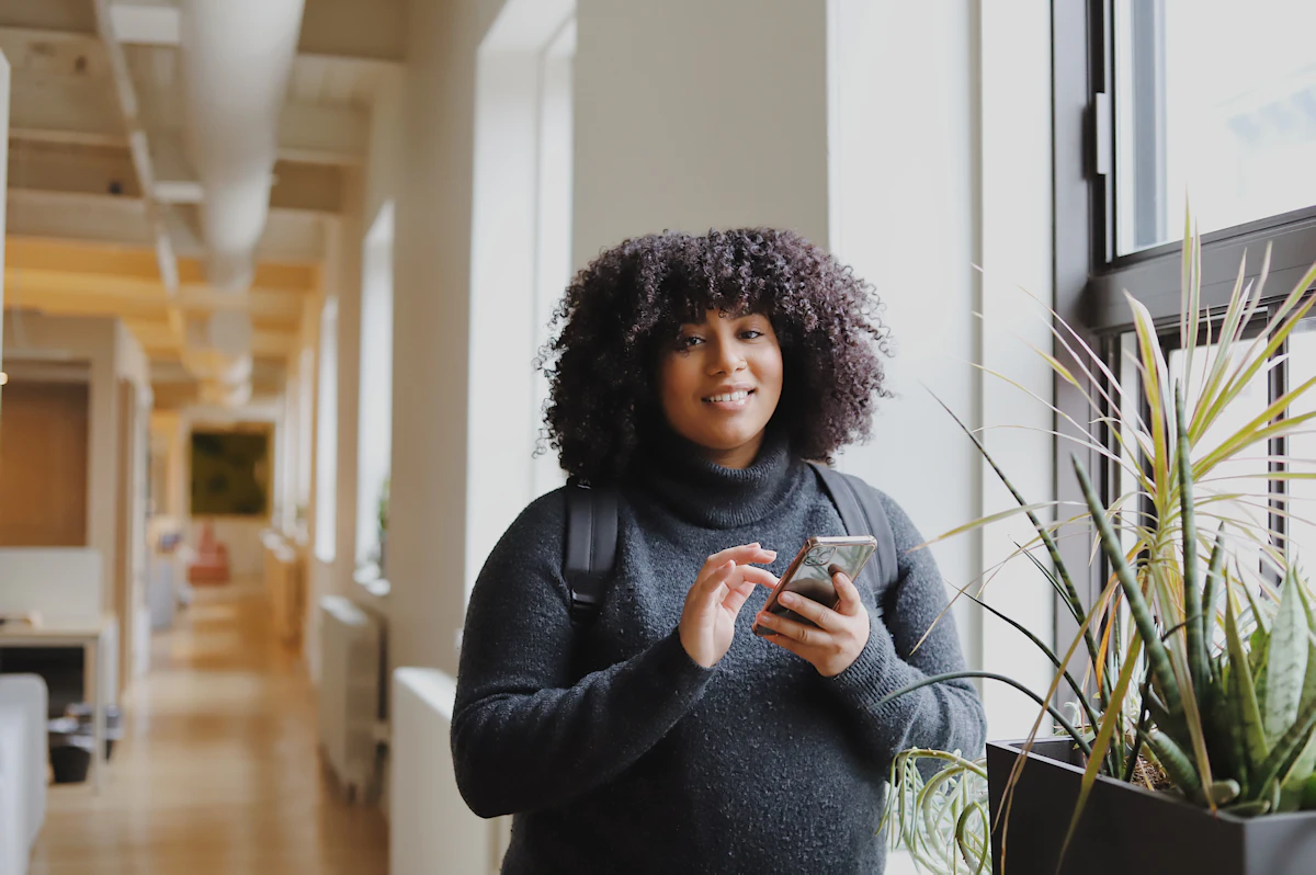 Black woman in business attire using a smartphone for WhatsApp customer communication and automation