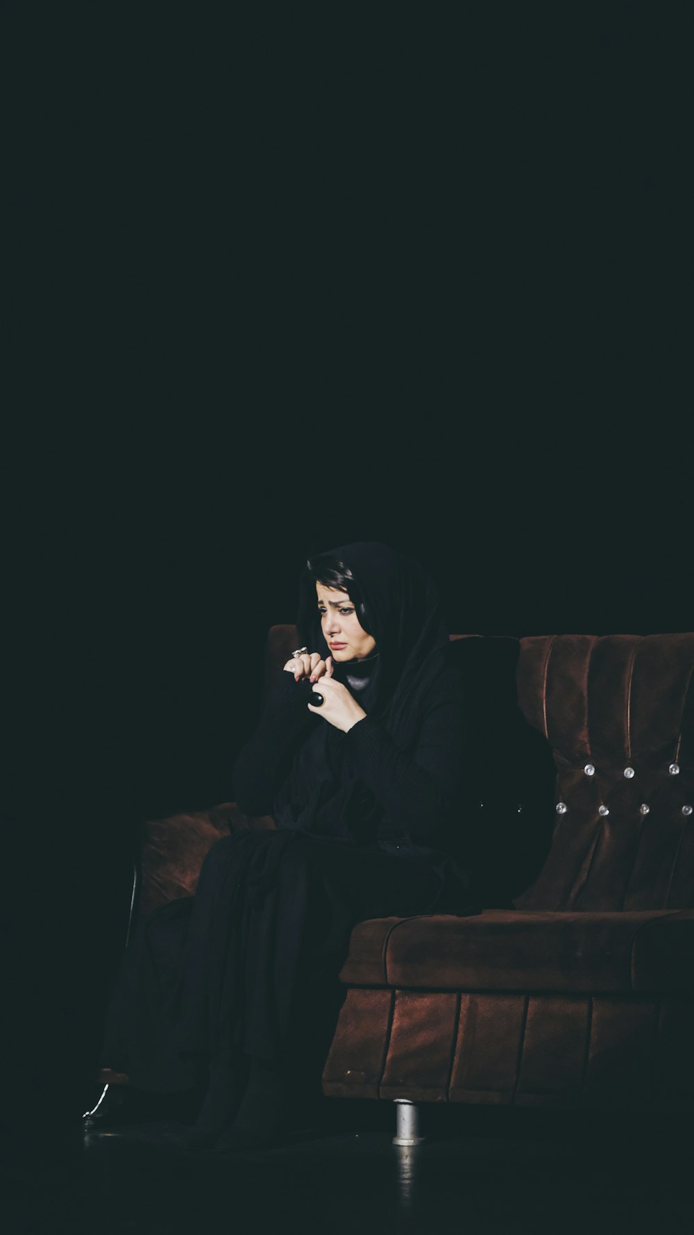 Femme en hijab noir assise sur un canapé marron