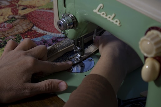 A person uses a vintage green sewing machine to stitch fabric with a colorful, patterned cloth. The focus is on the hands and the sewing process.