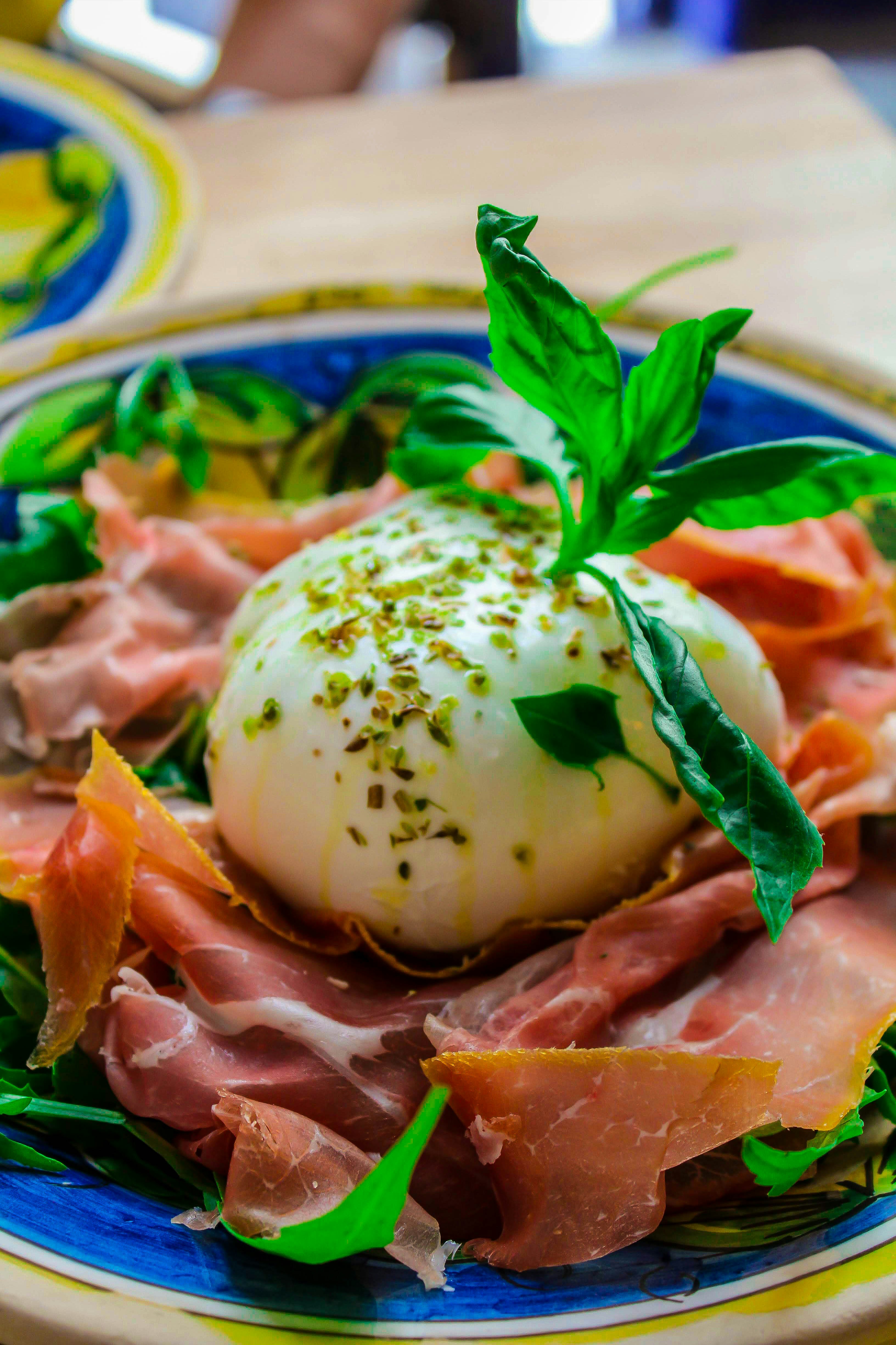 Fresh burrata cheese with prosciutto and arugula on a white plate