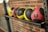 A row of four medicine balls neatly placed on a metallic rack against a brick wall. The balls are colored in yellow and red with black textured sections. Each ball is marked with weight measurements indicating 6 pounds on the red ball.