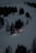 A snow plow is illuminated by its lights as it moves along a snow-covered mountain slope surrounded by tall, dark evergreen trees. The scene is set in a dimly lit, overcast environment, suggesting either dawn or dusk.