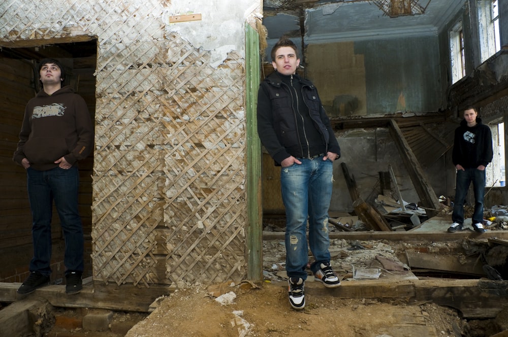 man in black jacket and blue denim jeans standing beside brown wooden door